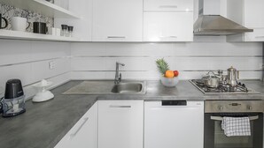 Een moderne keuken met witte kasten, een roestvrijstalen spoelbak, een koffiezetapparaat, een sapcentrifuge en een gasfornuis.