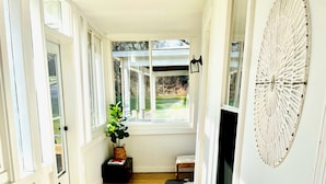 A bright hallway with wooden flooring, white walls, and large windows.