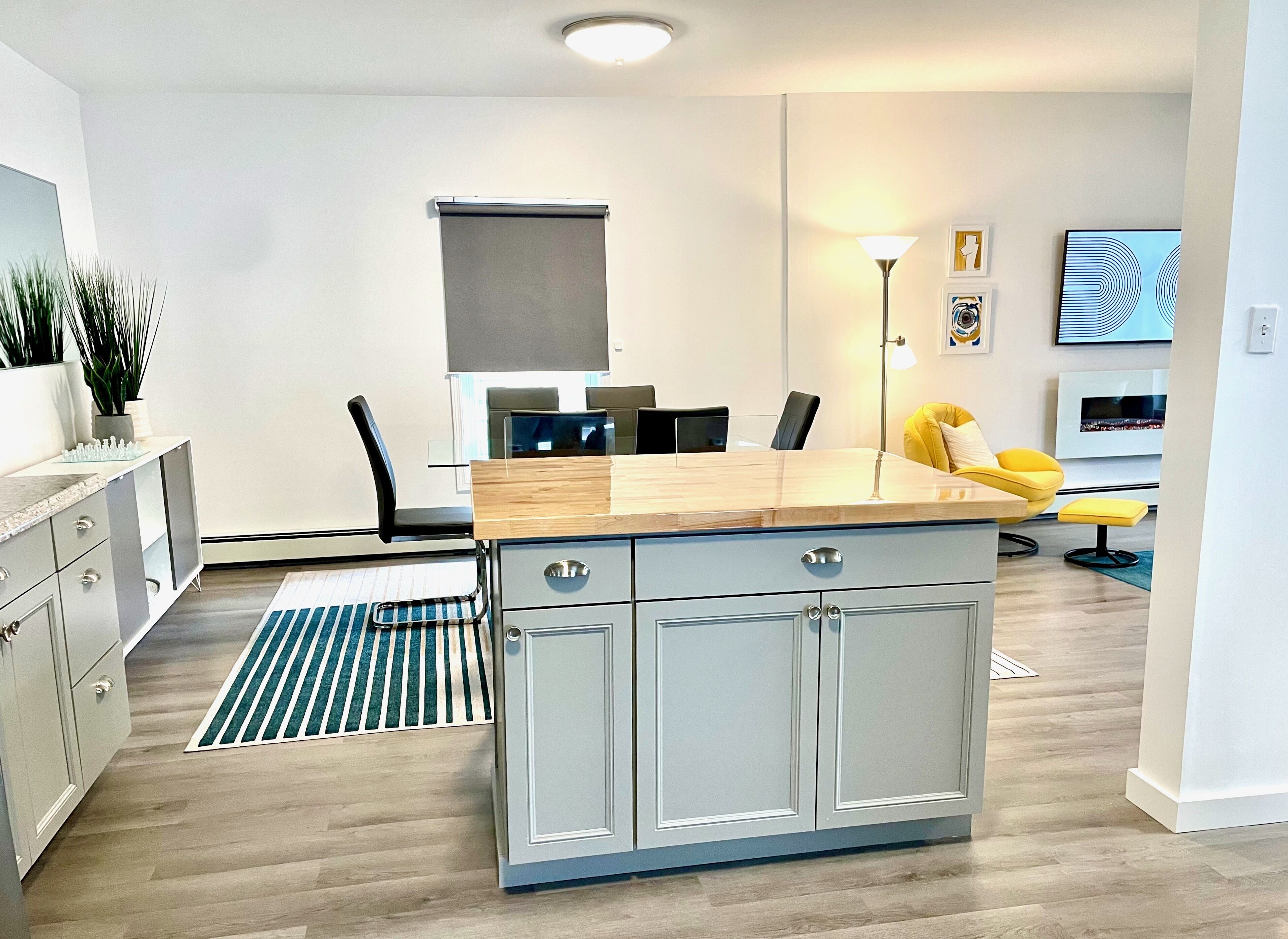 A modern kitchen with a central island, a dining area with chairs, a sofa, and a TV.
