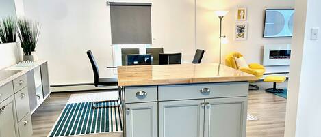A modern kitchen with a central island, a dining area with chairs, a sofa, and a TV.