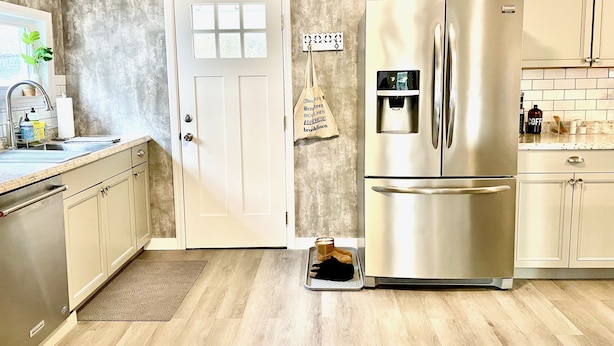 A kitchen with a stainless steel refrigerator, a sink, and a door with a window.