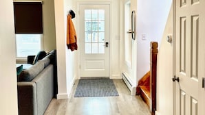 A hallway with a wooden floor, a white door, a coat rack, and a window with blinds.