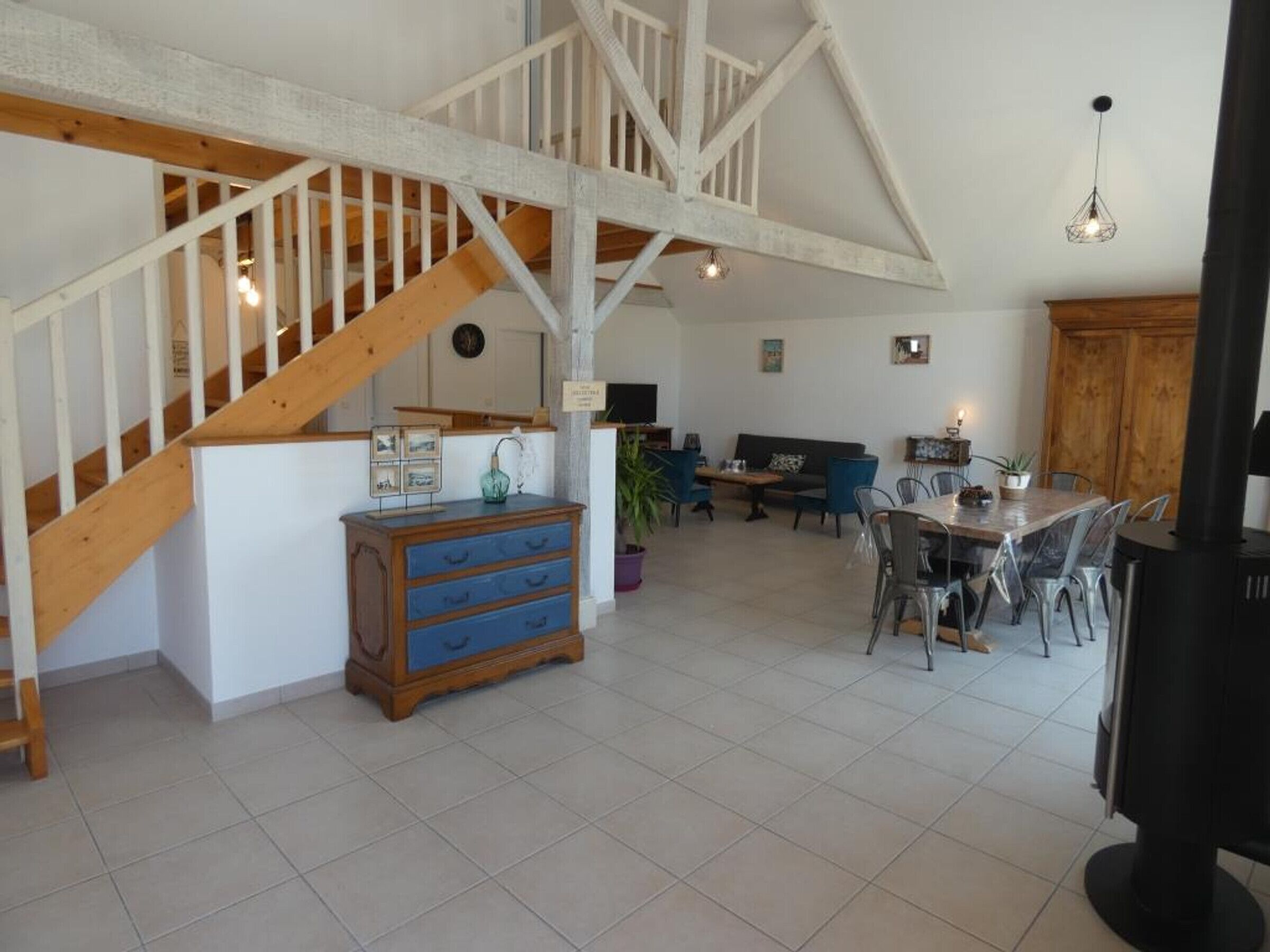 Amplia sala de estar con techo alto, escalera de madera y una mesa de comedor con sillas.