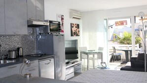 A modern kitchen with a microwave, stove, and dishwasher. There is a dining area with a glass table and chairs. - Cozy Studio with Pool Access, A/C, and Terrace in Port Ambonne (Cap d'Agde naturisme)