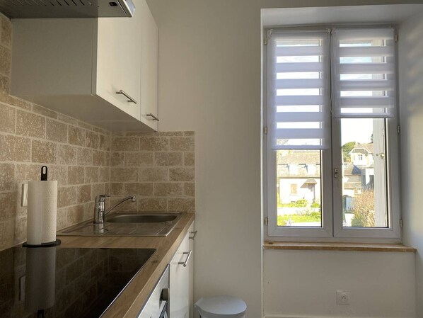 Una cocina con un lavamanos, una ventana con persianas y vistas al exterior.