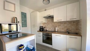 A modern kitchen with white cabinets, a microwave, a coffee maker, and a trash bin.