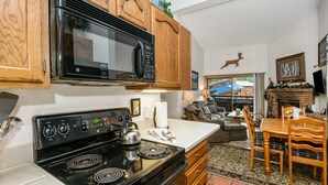 A kitchen with a stove, microwave, and wooden cabinets. There is a dining table with chairs and a fireplace.