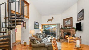 A cozy living room with a fireplace, a wooden staircase, and a comfortable seating area.