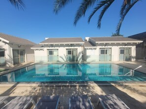 A rectangular swimming pool with a clear blue water surface, surrounded by a tiled deck. There are lounge chairs aligned along the pool's edge. - YalaRent Liri Resort - resort complex (Tiberias)