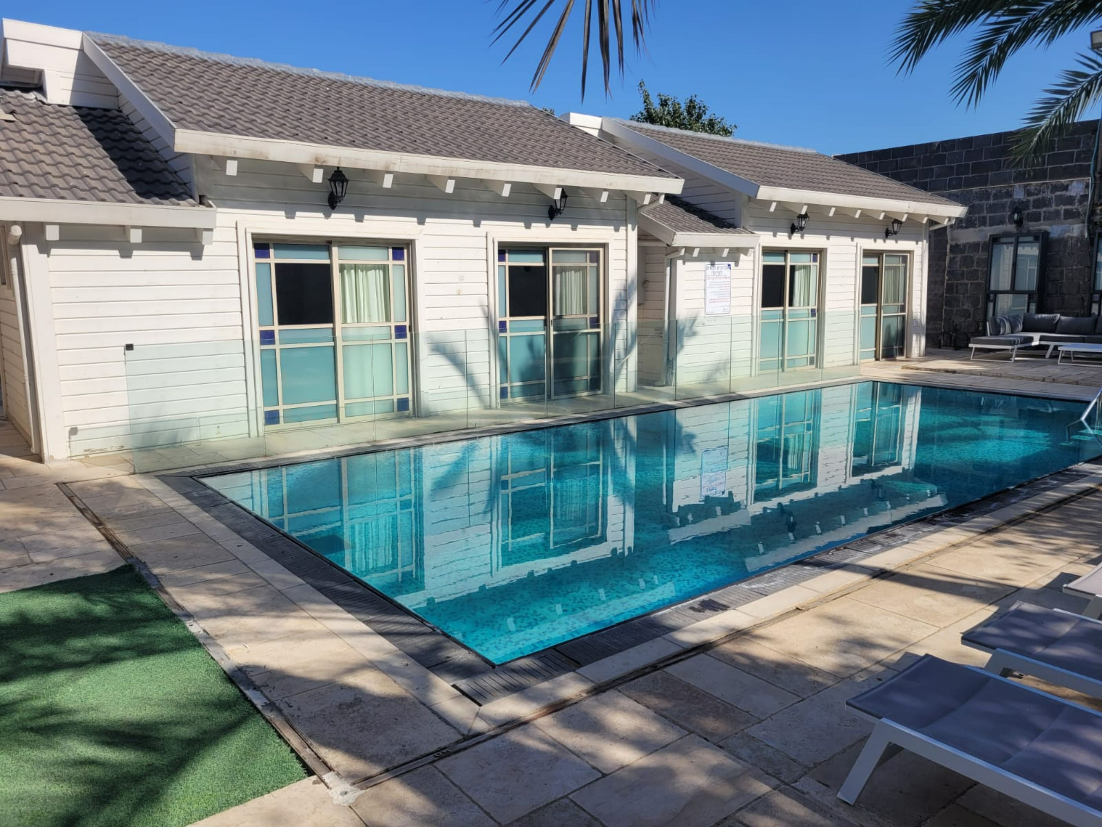 A poolside area with a swimming pool, lounge chairs, and a building with large windows and a tiled roof.