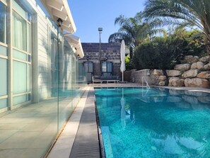 A swimming pool with clear blue water, a stone wall, and a palm tree.