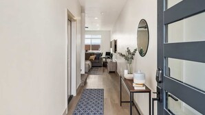Un couloir moderne avec un plancher en bois, un tapis à motifs, un canapé, une table basse et un miroir au mur.