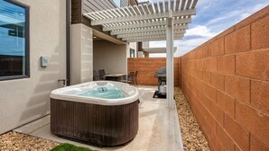Un bain à remous dans un jardin, agrémenté d’une pergola, d’un barbecue et d’une table de patio.