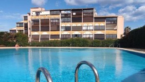 A swimming pool with metal ladders in the foreground and a multi-story building with balconies in the background. - Charming Studio for 4 with Pool Access, AC, and Parking - Close to Amenities (Cap d'Agde naturisme)