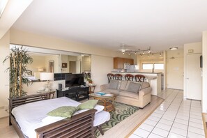 Quarto de hotel com cama, escrivaninha, televisão, sofá e cozinha.