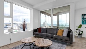 A modern living room with a grey sofa, two round wooden tables, and a city view through large windows. - Spacious 3BR apartment with 2 bathrooms (Reykjavík)