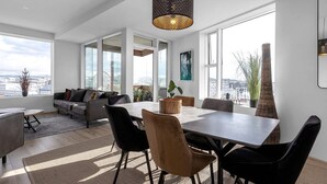 A modern living room with a large dining table, comfortable seating, and large windows offering a city view. - Spacious 3BR apartment with 2 bathrooms (Reykjavík)