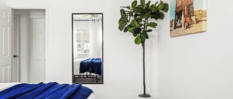 Un dormitorio con cama, espejo, planta en maceta y un cuadro en la pared.