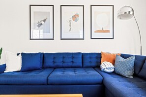 Un canapé bleu agrémenté de plusieurs coussins, un lampadaire et trois œuvres d’art encadrées accrochées au mur.