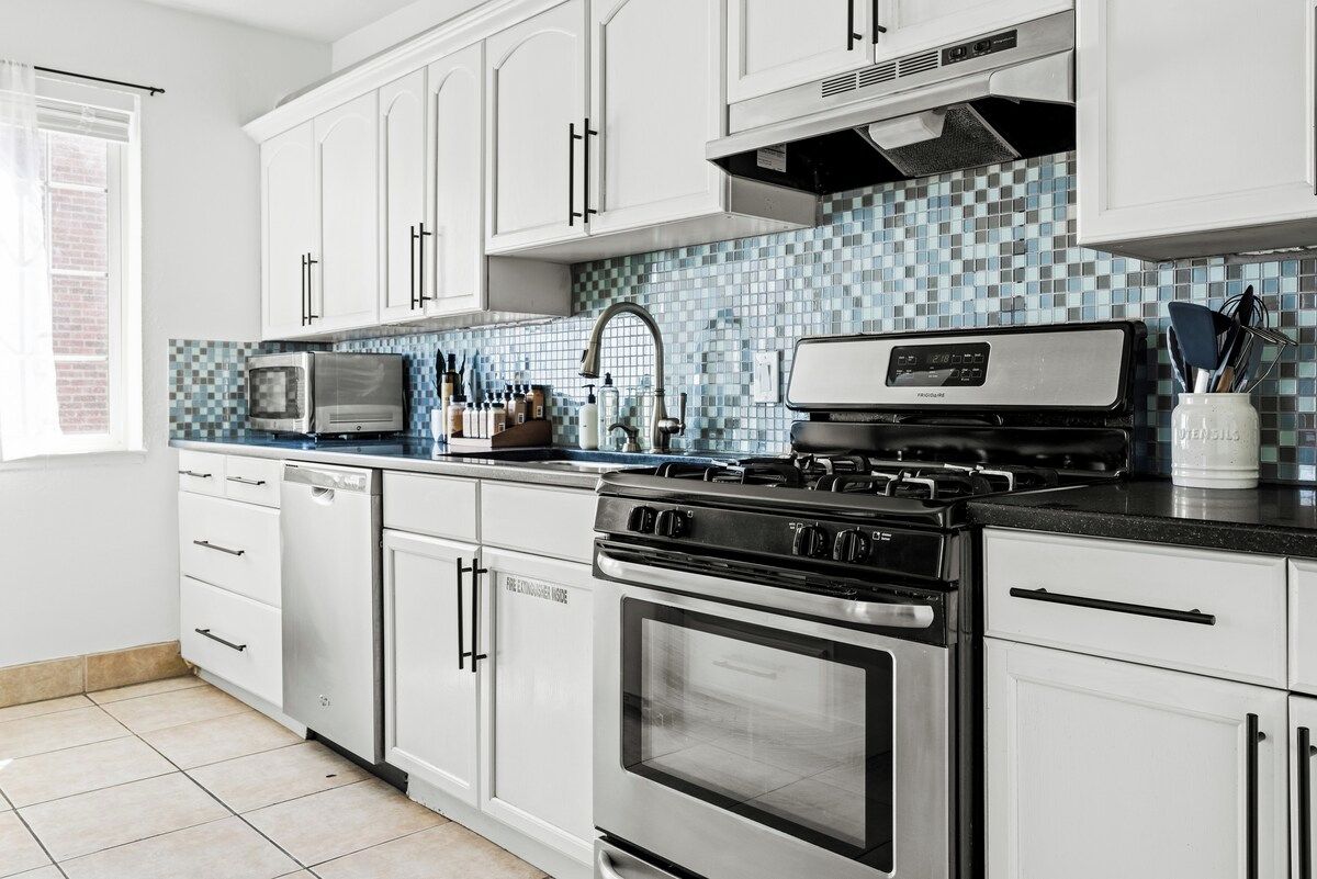 A kitchen with white cabinets, a microwave, a stove, and a tiled backsplash.