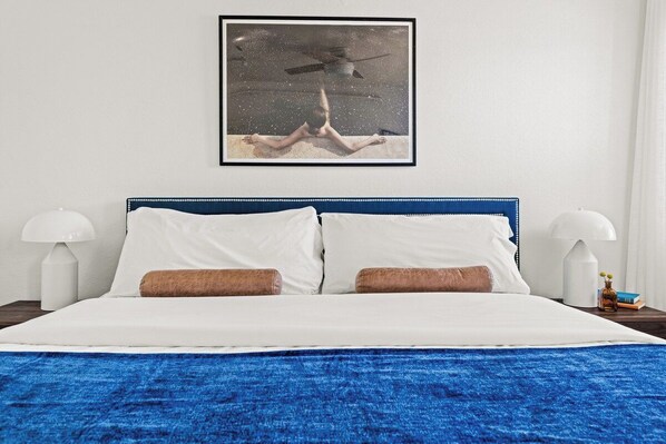 A bed with white and brown pillows, a blue headboard, and a framed picture above it.