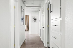 A hallway with white walls, wooden flooring, and doors with brass hinges.