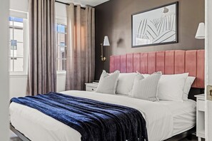 Habitación de hotel con una cama grande, cabecero, mesita de noche, lámpara y ventana con cortinas.
