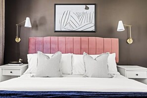 A bedroom with a pink headboard, white bedding, striped pillows, and two bedside lamps. - Modern Comfort | King Beds | Sloans Lake | 30 Day (Denver)