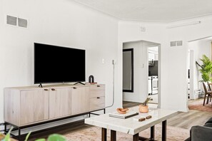 A modern living room with a flat-screen TV, a wooden cabinet, a marble coffee table, and a view into the kitchen. - Modern Comfort | King Beds | Sloans Lake | 30 Day (Denver)