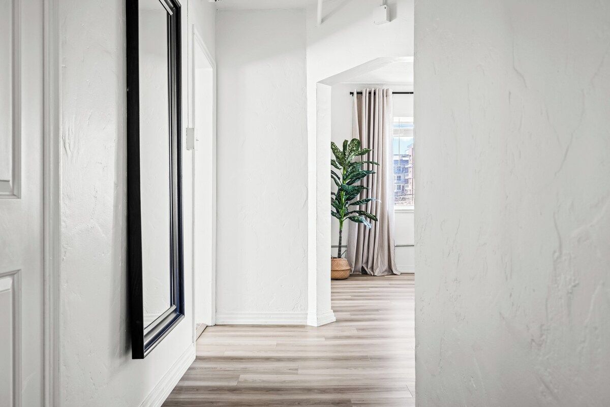 Ein Flur mit einem gerahmten Bild an der Wand, einem Blumentopf und Blick auf eine Stadtansicht durch ein Fenster.