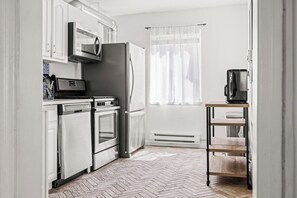 Una cocina con armarios blancos, un refrigerador de acero inoxidable, un microondas, una estufa y una máquina de café.