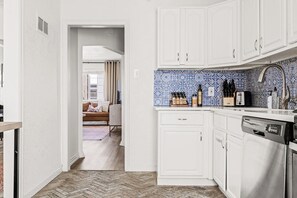 Una cocina compacta con muebles blancos, un salpicadero azul y blanco, y un lavavajillas.