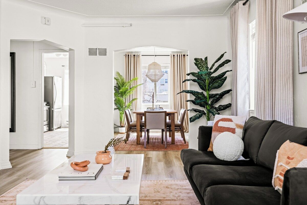 A modern living room with a dark sofa, a white coffee table, and a dining area with a table and chairs.