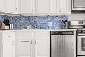 Una cocina con armarios blancos, lavavajillas, horno y salpicadero con azulejos azules y blancos.