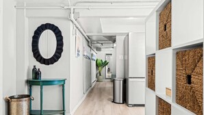 A hallway with a teal table, a metal trash can, a mirror, and a refrigerator. - Contemporary Studio Near Sloan's Lake | 30 Day (Denver)