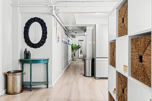 A hallway with a teal table, a metal trash can, a mirror, and a refrigerator. - Contemporary Studio Near Sloan's Lake | 30 Day (Denver)