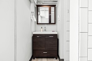 A narrow bathroom with a dark wooden vanity, white countertop, and a mirror above the sink. - Contemporary Studio Near Sloan's Lake | 30 Day (Denver)