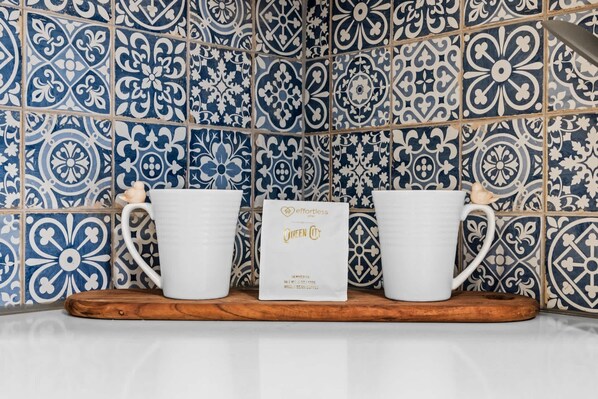 Two white ceramic mugs on a wooden tray against a tiled wall with blue and white patterns.
