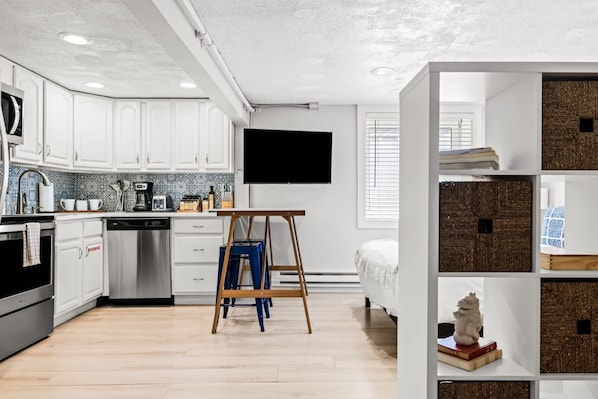 A modern kitchen with white cabinets, a wooden table, and a TV mounted on the wall.