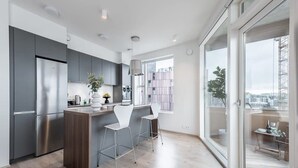 Une cuisine moderne dotée d’un îlot central, d’appareils électroménagers en acier inoxydable et offrant une vue sur la ville grâce à de grandes fenêtres.