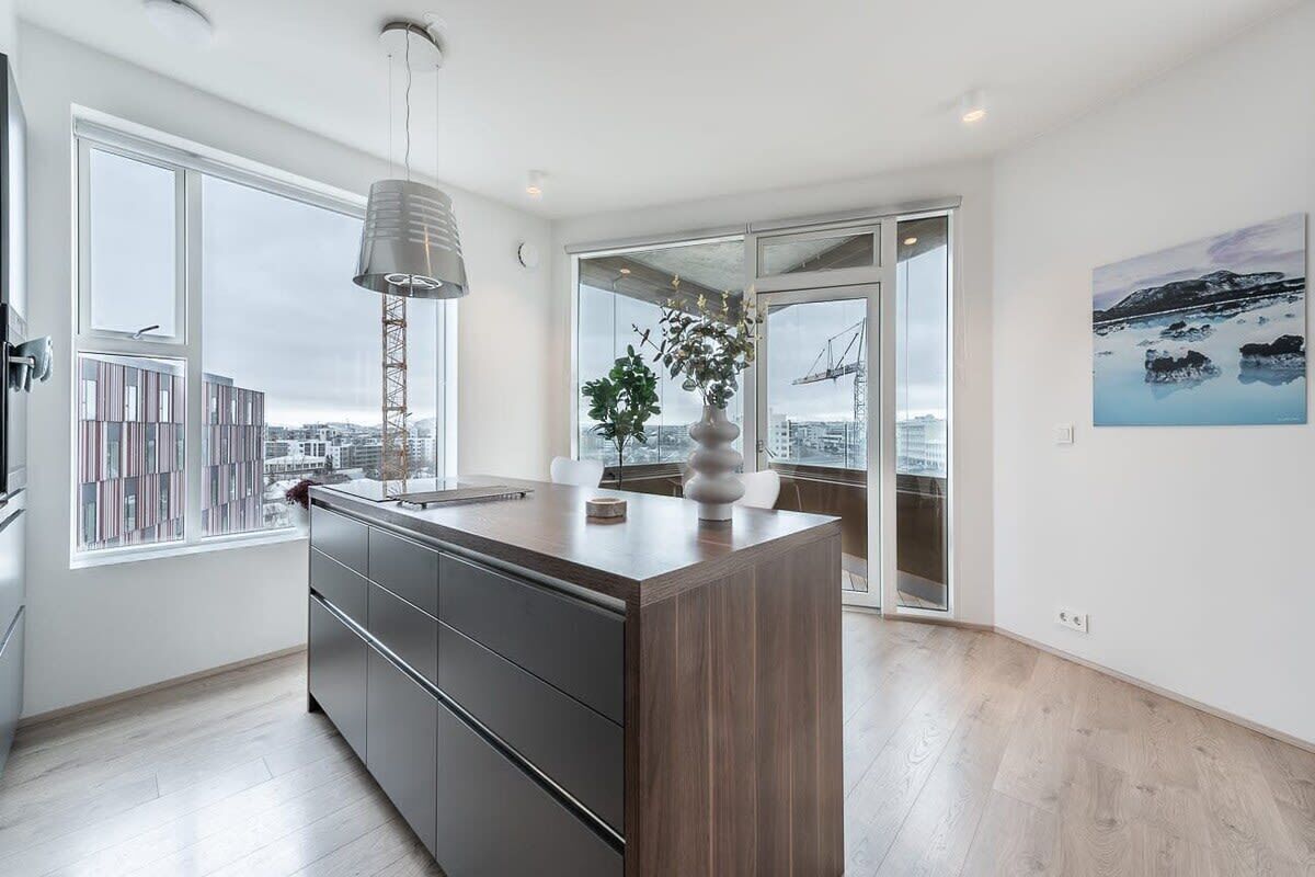 Una cocina moderna con una isla grande, una lámpara colgante y vistas a la ciudad a través de ventanas amplias.