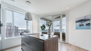 Une cuisine moderne dotée d’un grand îlot central, d’un luminaire suspendu et offrant une vue sur la ville grâce à de grandes fenêtres.