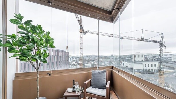 Un balcon donnant sur la ville, une plante en pot, une table avec une bouteille et une chaise.