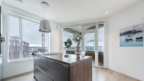 Una cocina moderna con una isla grande, una lámpara colgante y vistas a la ciudad a través de ventanas amplias.