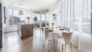 A modern kitchen with a central island, a dining area with a round table and chairs, and large windows offering a city view.