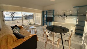 A modern living room with a sofa, dining table, chairs, and a kitchen area with blue cabinets and a TV. - Ground floor apartment, 4 people, pool, beach 200 m, wifi (Fouras)