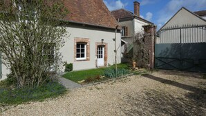 Une maison à deux étages avec une façade en briques, un petit jardin à l’avant et une allée gravillonnée.