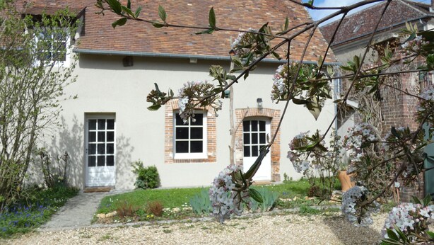 Un bâtiment avec un toit en briques et des murs blancs, entouré de gravier et de plantes.
