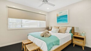 Una camera da letto con un letto, due poltrone in vimini, un comodino, una finestra e una ventola a soffitto.