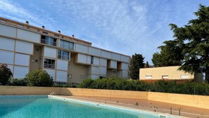 Une piscine dotée d’une terrasse carrelée, entourée d’un petit muret et bordée d’un immeuble comportant plusieurs balcons.